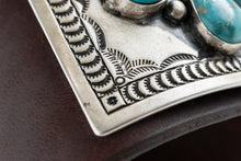 Load image into Gallery viewer, Close up of the intricate hand stamp work on the silver portion of a dark brown leather bow guard with nine turquoise stones