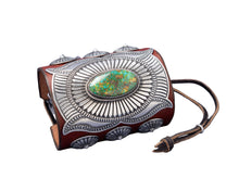 Load image into Gallery viewer, A handcrafted leather bowguard featuring an elaborate stamped sterling silver overlay with a radiant sunburst design, centered around a vibrant Sonoran Gold turquoise cabochon. Accented with scalloped conchos on the sides and a brown leather strap for fastening.