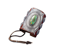 Load image into Gallery viewer, A handcrafted leather bowguard featuring an elaborate stamped sterling silver overlay with a radiant sunburst design, centered around a vibrant Sonoran Gold turquoise cabochon. Accented with scalloped conchos on the sides and a brown leather strap for fastening.