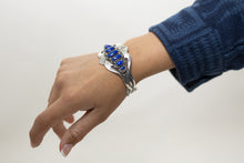 Load image into Gallery viewer, Model wearing a silver stamped bracelet with blue stones on a plain background