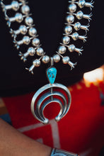 Load image into Gallery viewer, A close-up image of a silver Navajo Squash Blossom necklace with Morenci Turquoise Gemstones around a person's neck.
