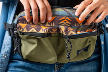 Load image into Gallery viewer, Two hands holding a Pendleton green patterned waist bag with a visible brand logo.