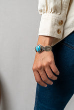 Load image into Gallery viewer, Hand wearing a silver Terry Martinez bracelet with a turquoise stone against a neutral background