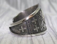 Load image into Gallery viewer, handcrafted silver cuff bracelet featuring intricate geometric and cross patterns etched into the metal. The design is bold and symmetrical, with a textured background that enhances the detailed craftsmanship. The bracelet rests on a neutral surface, emphasizing its artistic and traditional appeal.