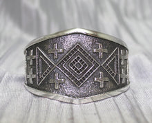 Load image into Gallery viewer, handcrafted silver cuff bracelet featuring intricate geometric and cross patterns etched into the metal. The design is bold and symmetrical, with a textured background that enhances the detailed craftsmanship. The bracelet rests on a neutral surface, emphasizing its artistic and traditional appeal.