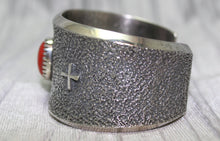 Load image into Gallery viewer, A wide silver cuff bracelet with a textured surface, small silver cross on side. The cuff rests on a soft gray background, highlighting its intricate craftsmanship.