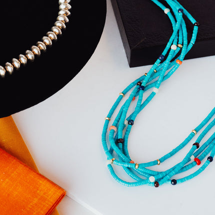 Turquoise necklace and silver beaded necklace laying out on black and white square boxes