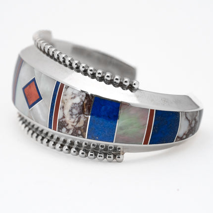 A silver bracelet with geometric inlay patterns including lapis, mother-of-pearl, and abalone, accented with coral lines and polished silver beads.