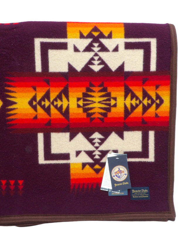 Pendleton Chief Joseph Blanket in Maroon featuring a traditional Native American-inspired geometric pattern with arrow motifs, folded neatly to show intricate design and soft wool texture. Front view