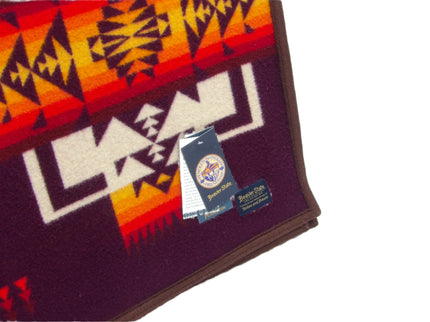 Pendleton Chief Joseph Blanket in Maroon featuring a traditional Native American-inspired geometric pattern with arrow motifs, folded neatly to show intricate design and soft wool texture, tag view