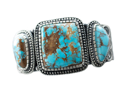 Center close up of Royston Turquoise with brown matrix, in center of silver bracelet by Navajo Silversmith Matthew Charley, on a solid white background. 