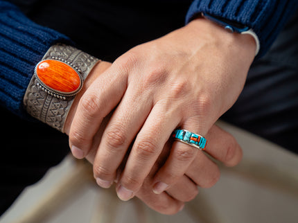 Close-up of hands wearing a silver bracelet with an orange stone and a turquoise cobble inlay ring