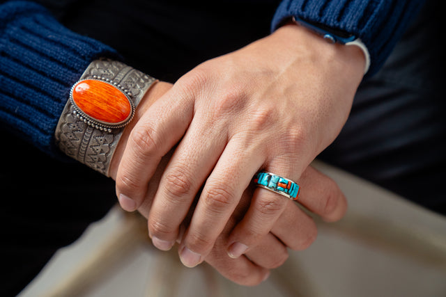 Close-up of hands wearing a silver bracelet with an orange stone and a turquoise cobble inlay ring