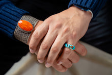 Load image into Gallery viewer, Close-up of hands wearing a silver bracelet with an orange stone and a turquoise cobble inlay ring

