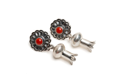 Pair of silver earrings with a single coral stone in the center of silver shaped like a blossom on a white background