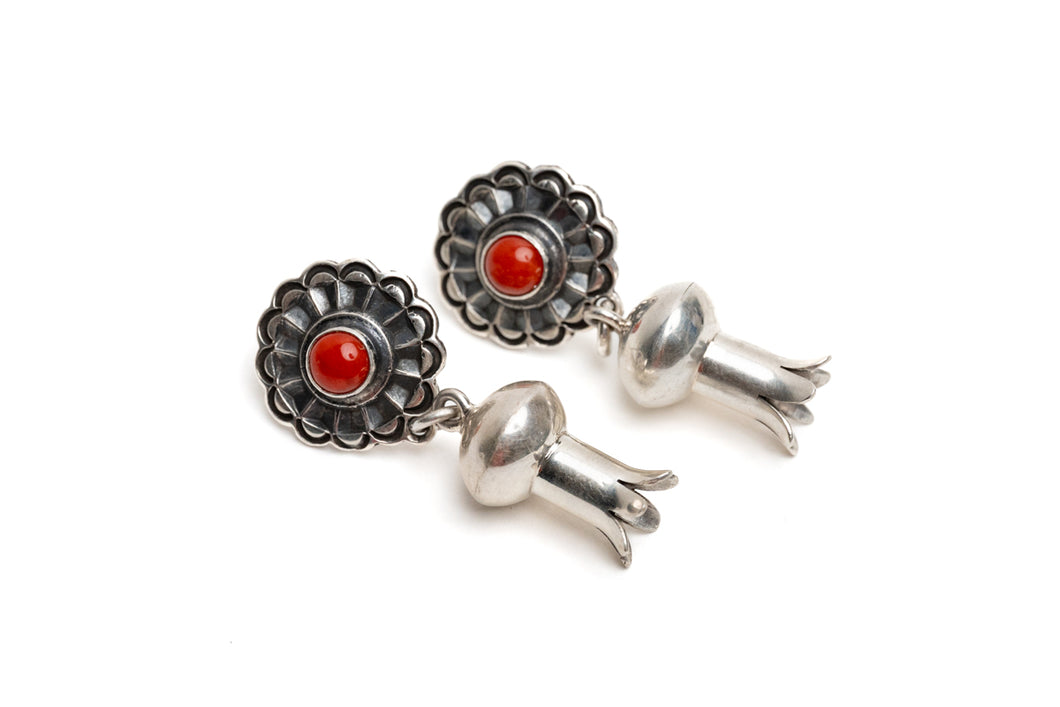 Pair of silver earrings with a single coral stone in the center of silver shaped like a blossom on a white background