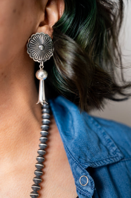 Close-up of a drop earring with a tassel hanging from an ear, wearing a blue shirt.