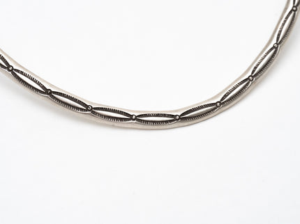 close up of stamp lines on a silver choker necklace on a white background