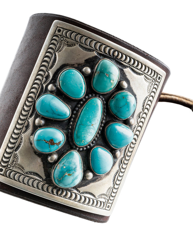 Dark brown leather bow guard with nine turquoise stones on a silver plate with stamp work on a white background