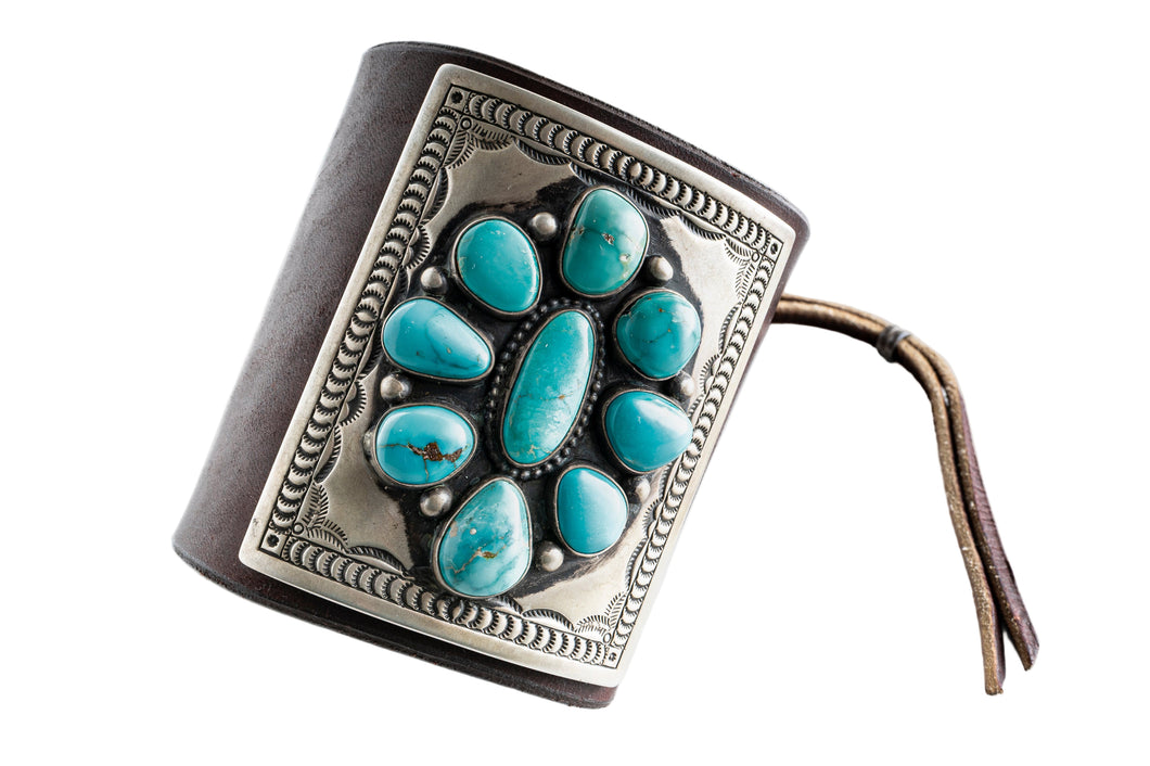 Dark brown leather bow guard with nine turquoise stones on a silver plate with stamp work on a white background
