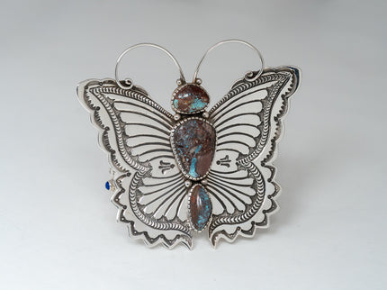 Front side of bracelet showcasing a large silver butterfly with antennas and three turquoise stones.