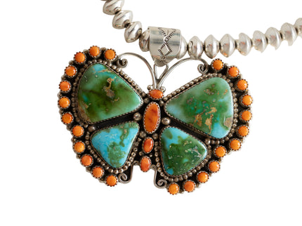 Butterfly-shaped pendant with turquoise stones and orange accents on a white background
