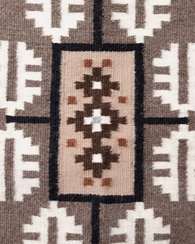 Close up of a Navajo handwoven rug with geometric pattern featuring brown, beige, and white colors.