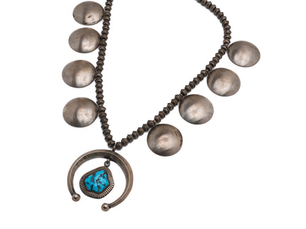 An old fashioned Navajo squash blossom necklace with eight silver discs a large turquoise stone at the center