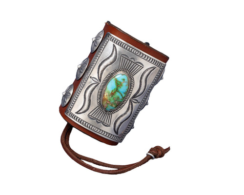 A richly detailed leather bowguard with a rectangular sterling silver plate showcasing flowing stamped patterns and a striking green-blue Sonoran Gold turquoise stone at the center. Decorated with dome-shaped silver conchos and secured with a dark brown leather tie.