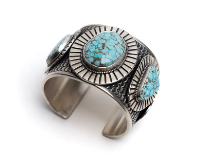 Silver cuff bracelet with 3 number eight turquoise stones on a white background