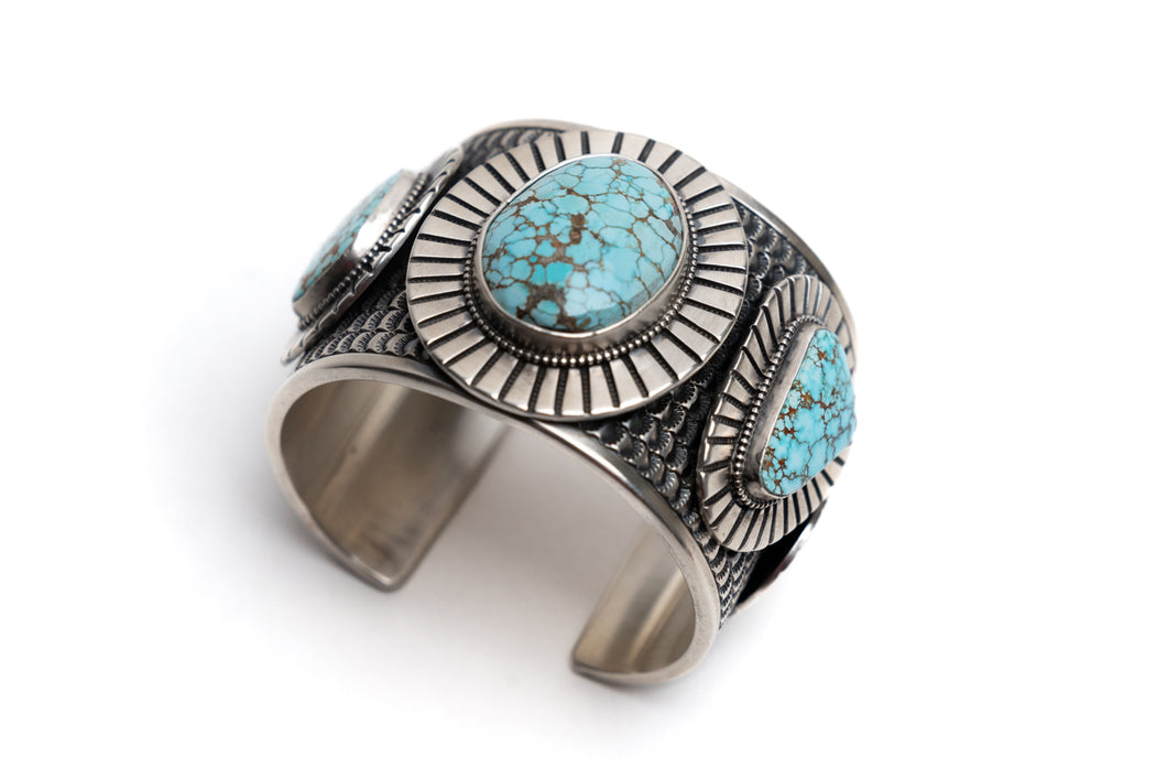 Silver cuff bracelet with 3 number eight turquoise stones on a white background
