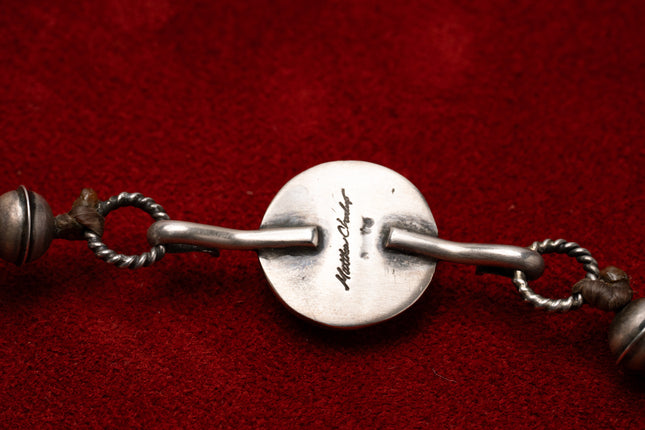 Close up of the name Matthew Charlie stamped into a silver necklace on a red background 