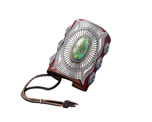 A handcrafted leather bowguard featuring an elaborate stamped sterling silver overlay with a radiant sunburst design, centered around a vibrant Sonoran Gold turquoise cabochon. Accented with scalloped conchos on the sides and a brown leather strap for fastening.