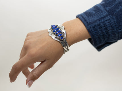 Model wearing a silver stamped bracelet with blue stones on a plain background
