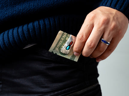 Hand with a blue ring holding a twenty dollar bill with a silver and turquoise money clip