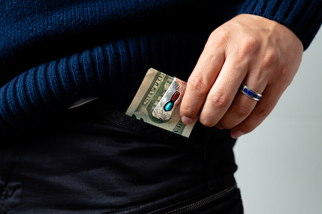 Hand with a blue ring holding a twenty dollar bill with a silver and turquoise money clip