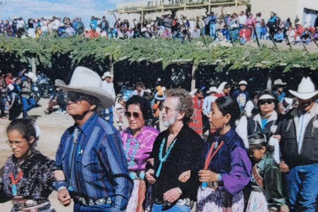Ellis Tanner wearing a black long sleeve shirt and dancing in between two older Navajo women. The background is filled with Navajo spectators as other Navajos dance for Native American Appreciation Day