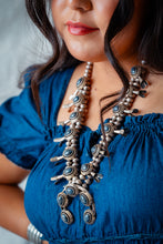 Load image into Gallery viewer, Navajo woman wearing a blue dress and a detailed Navajo squash blossom necklace with blue gem stones.

