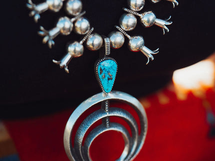 A close-up image of a silver Navajo Squash Blossom necklace with Morenci Turquoise Gemstones around a person's neck.