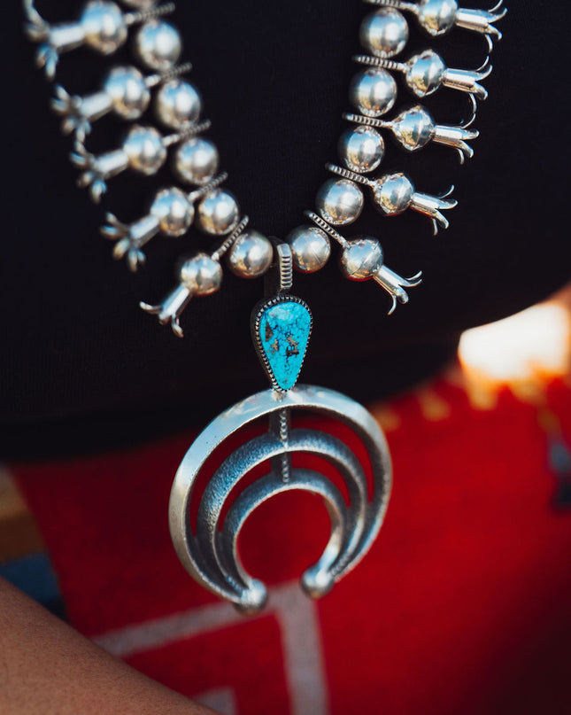 A close-up image of a silver Navajo Squash Blossom necklace with Morenci Turquoise Gemstones around a person's neck.
