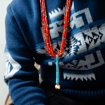 Person wearing a blue Pendleton sweater with a coral jacloo necklace.