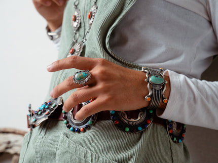 Navajo woman wearing multiple pieces of jewelry including an old-fashioned  Turquoise ring, a silver bracelet, and a concho on a light background