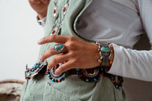 Load image into Gallery viewer, Navajo woman wearing multiple pieces of jewelry including an old-fashioned  Turquoise ring, a silver bracelet, and a concho on a light background
