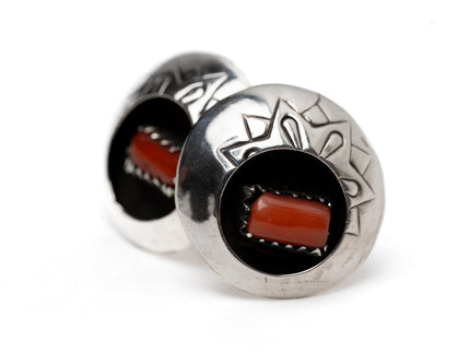 Pair of circular Native American silver and coral shadow box earrings leaning against each other on a white background