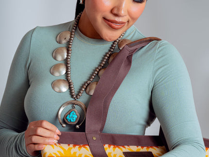 Young Adults Navajo Woman wearing a long-sleeve green t-shirt and is holding a Pendleton Tote. She is wearing a large turquoise butterfly ring on her left hand