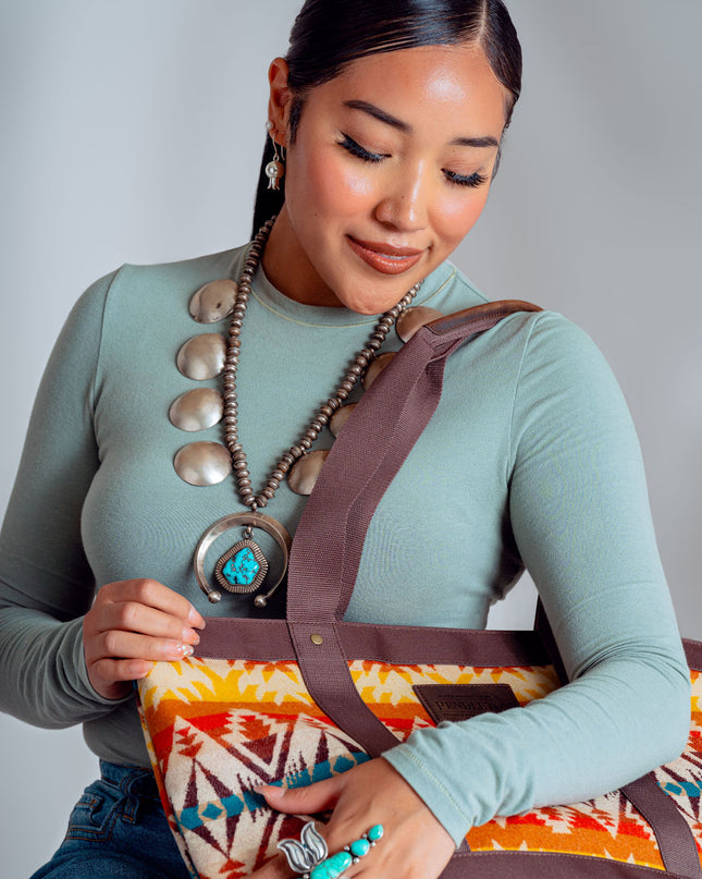 Young Adults Navajo Woman wearing a long-sleeve green t-shirt and is holding a Pendleton Tote. She is wearing a large turquoise butterfly ring on her left hand