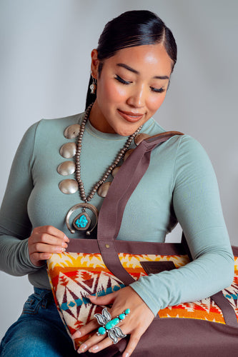 Young Adults Navajo Woman wearing a long-sleeve green t-shirt and is holding a Pendleton Tote. She is wearing a large turquoise butterfly ring on her left hand