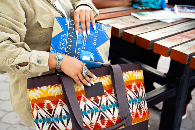 A Navajo female student is putting a tote bag by Pendleton and placing a book inside of it