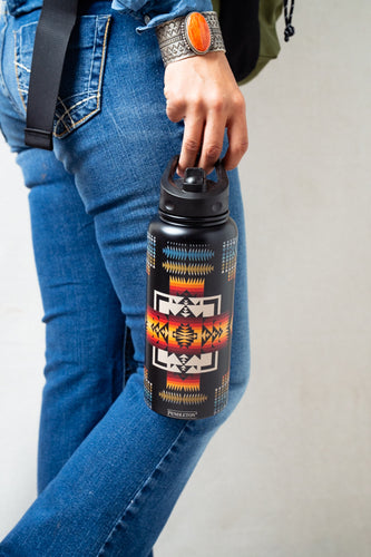 Person holding a water bottle with a colorful pattern, wearing blue jeans and an orange turquoise bracelet.