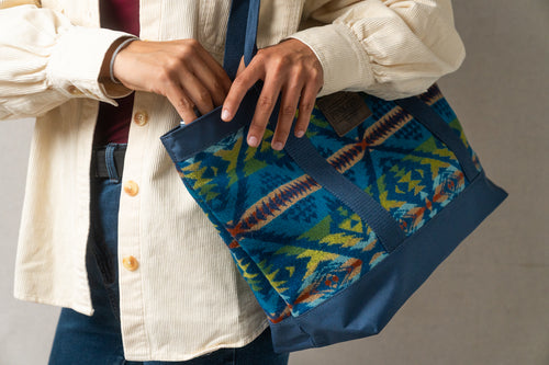 Person wearing a cream color Levi button up shirt is holding a blue and multicolored Pendleton patterned bag